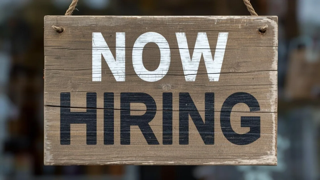 A weathered wooden “Now Hiring” sign.